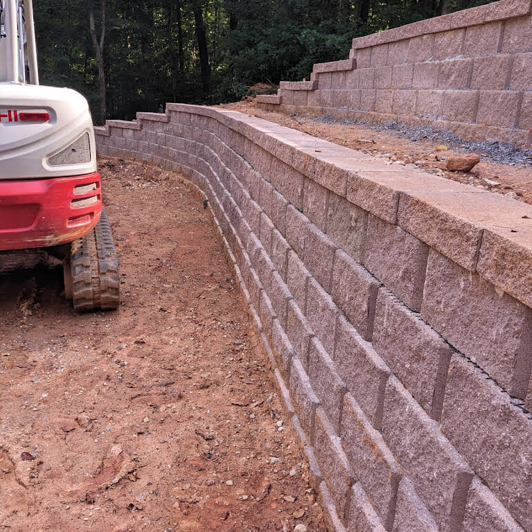 Long curved terraced block retaining wall along an access drive with excavator on site